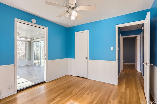 empty room with attic access, wood finished floors, a wainscoted wall, and ceiling fan