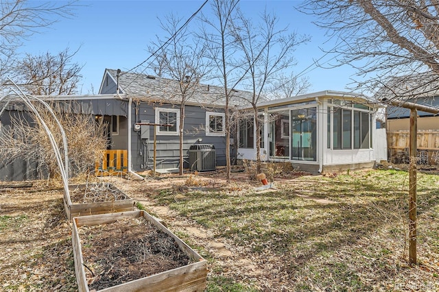 rear view of house with central AC unit, a sunroom, a vegetable garden, and fence