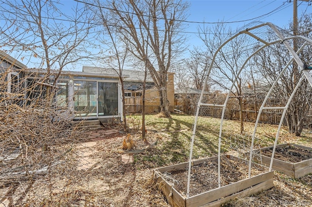 view of yard featuring a garden, fence, and a sunroom