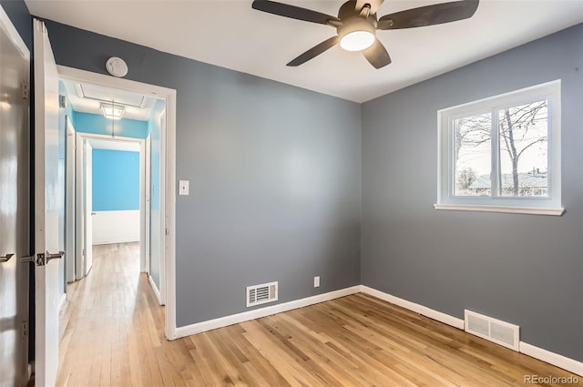 empty room featuring attic access, light wood-style floors, a ceiling fan, baseboards, and a smoke detector