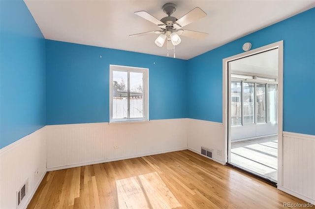 unfurnished room featuring a wainscoted wall, wood finished floors, and a ceiling fan