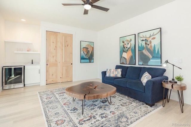 living room featuring ceiling fan, beverage cooler, light hardwood / wood-style floors, and indoor wet bar