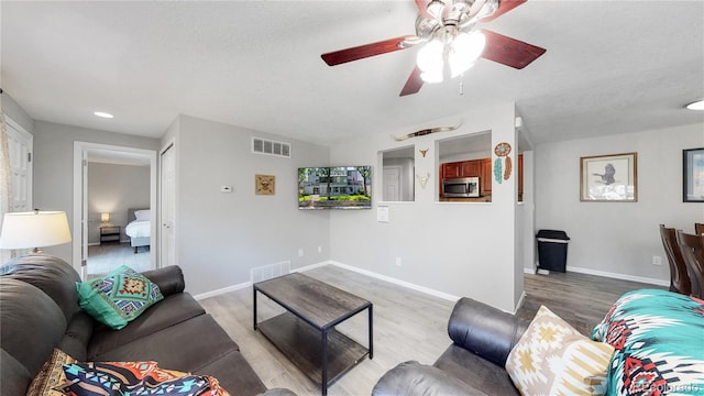 living room with ceiling fan, a textured ceiling, and light hardwood / wood-style flooring