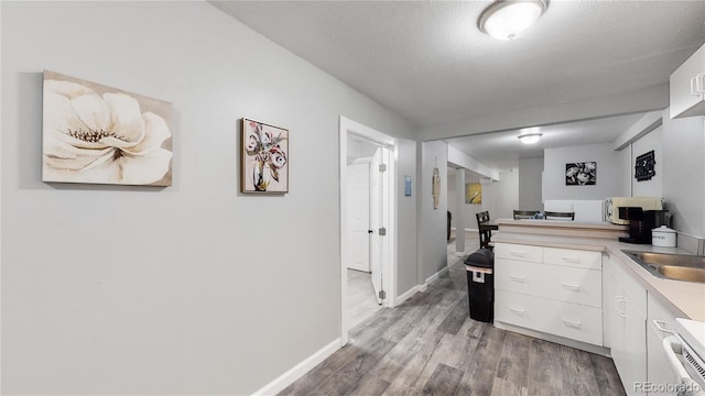 kitchen featuring sink, white cabinetry, a textured ceiling, light hardwood / wood-style floors, and kitchen peninsula