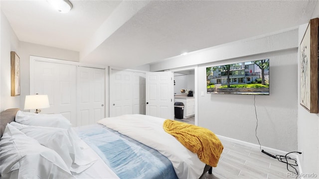 bedroom with a textured ceiling, two closets, and light hardwood / wood-style flooring