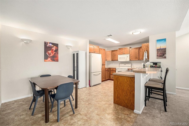 10818 Cimarron St Unit 206, Firestone, CO 80504 - kitchen featuring white appliances, a peninsula, light countertops, a breakfast bar, and baseboards