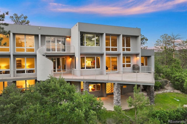 back house at dusk featuring a balcony and a patio