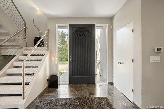 foyer with marble finish floor, stairs, and baseboards