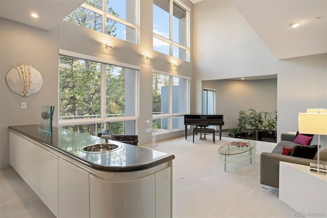 kitchen featuring white cabinets, light colored carpet, a towering ceiling, modern cabinets, and a sink