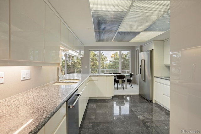 kitchen with appliances with stainless steel finishes, plenty of natural light, a sink, and light stone countertops