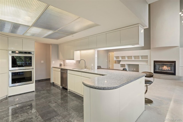 kitchen featuring double oven, a glass covered fireplace, open floor plan, a sink, and a peninsula