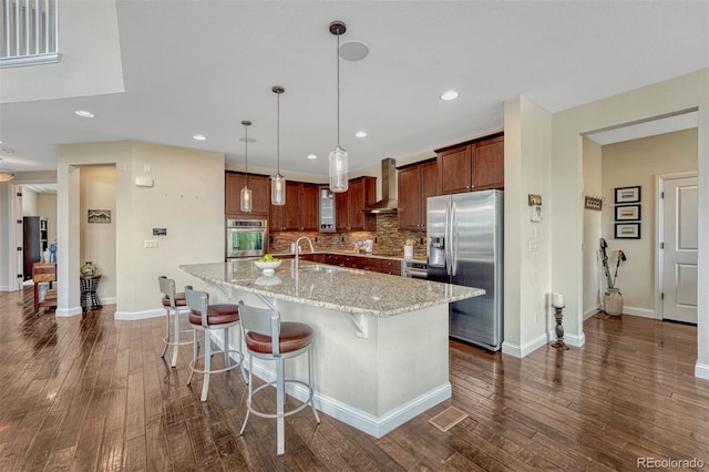 10365 Prairie Sky Pl, Lone Tree, CO 80124 - kitchen featuring stainless steel appliances, wall chimney range hood, dark wood finished floors, decorative backsplash, and a kitchen breakfast bar