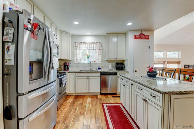 8555 Angela Ln, Parker, CO 80134 - kitchen featuring stainless steel appliances, a sink, light wood-style floors, decorative backsplash, and a center island