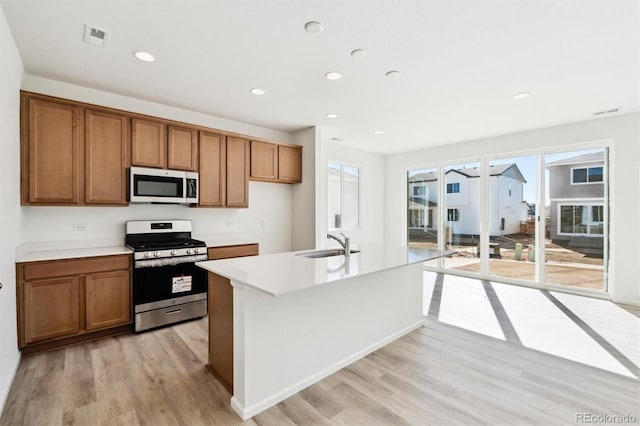 kitchen with a sink, stainless steel appliances, light wood-type flooring, and brown cabinetry