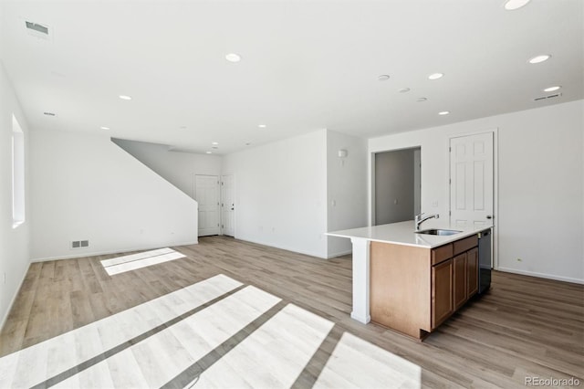 kitchen with dishwashing machine, a center island with sink, visible vents, a sink, and light wood-type flooring