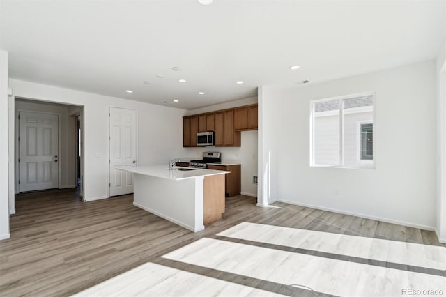 kitchen featuring light wood-style flooring, an island with sink, light countertops, appliances with stainless steel finishes, and brown cabinets