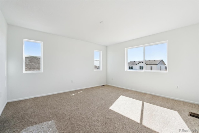 unfurnished room with a wealth of natural light, visible vents, baseboards, and carpet floors