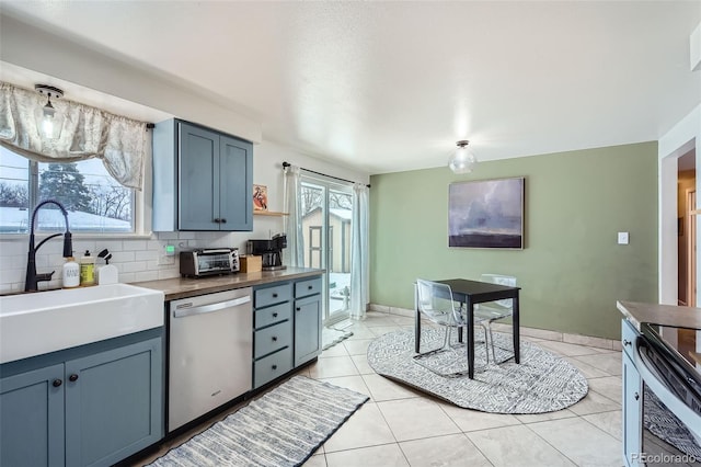 kitchen with light tile patterned flooring, tasteful backsplash, dishwasher, sink, and blue cabinetry