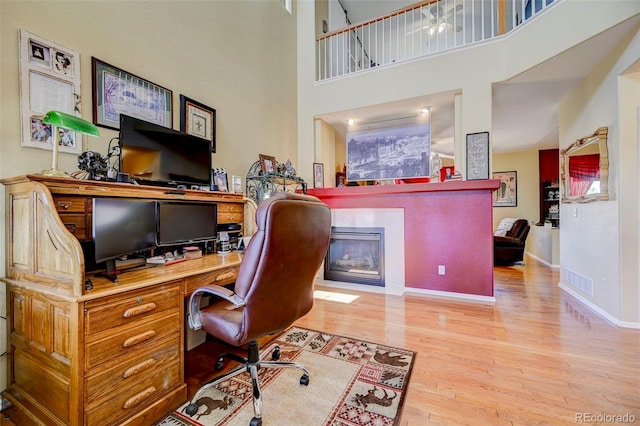 9172 Sunningdale Rd, Peyton, CO 80831 - home office with baseboards, a fireplace with flush hearth, wood finished floors, a towering ceiling, and visible vents