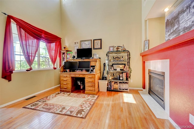 9172 Sunningdale Rd, Peyton, CO 80831 - home office with hardwood / wood-style floors, baseboards, a fireplace with flush hearth, a towering ceiling, and visible vents