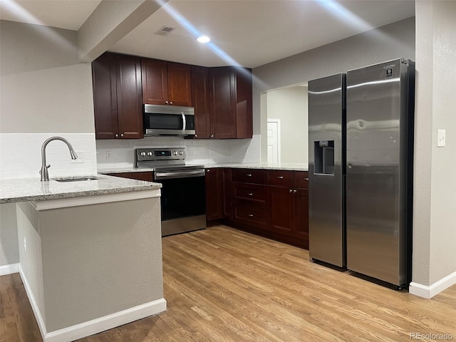 kitchen featuring light stone countertops, sink, backsplash, kitchen peninsula, and appliances with stainless steel finishes