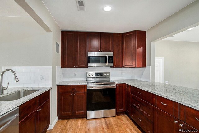 3092 S Kearney St, Denver, CO 80222 - kitchen featuring appliances with stainless steel finishes, a sink, reddish brown cabinets, light wood-style flooring, and light stone countertops