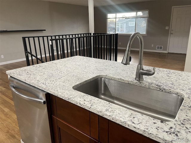 kitchen with stainless steel dishwasher, light stone countertops, sink, and hardwood / wood-style floors