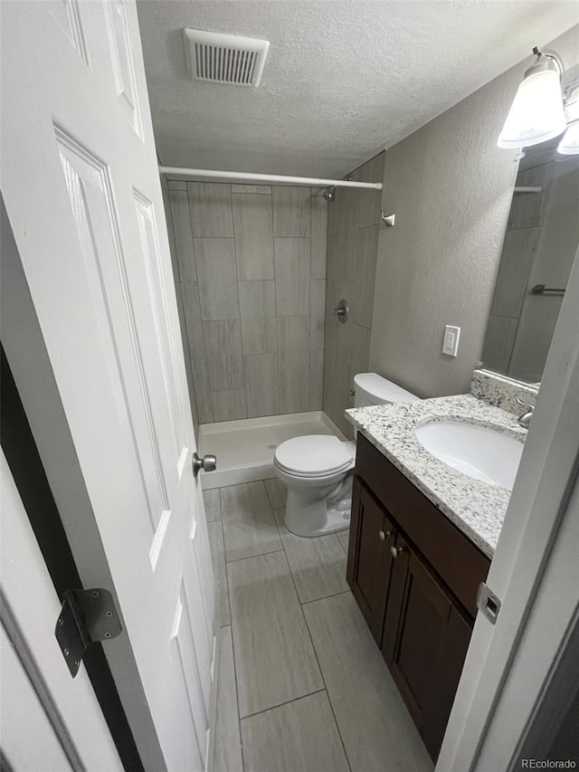 bathroom featuring a tile shower, vanity, a textured ceiling, and toilet