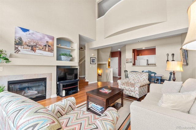 living room featuring a fireplace, wood-type flooring, a towering ceiling, and built in features