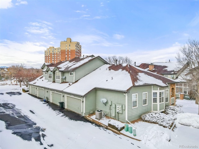 snow covered back of property featuring a garage and central air condition unit