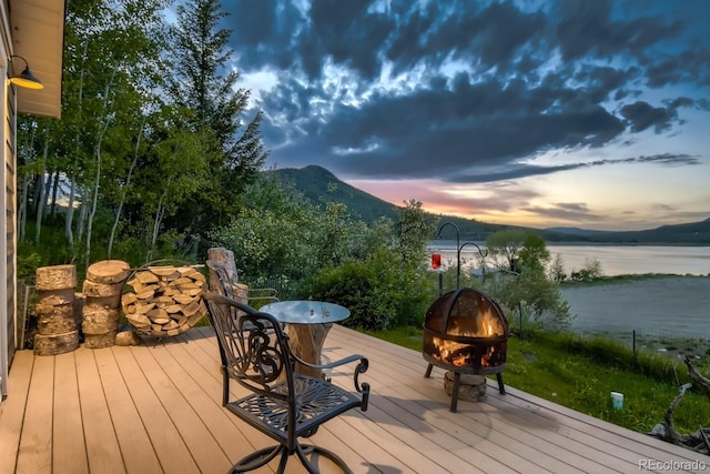 deck at dusk with a grill, a water and mountain view, and an outdoor fire pit