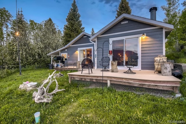 rear view of property featuring a wooden deck, an outdoor fire pit, and a lawn