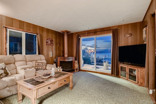 living room with carpet floors, wooden walls, and a wood stove