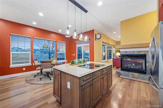 kitchen with a tiled fireplace, black electric stovetop, light wood-type flooring, and freestanding refrigerator