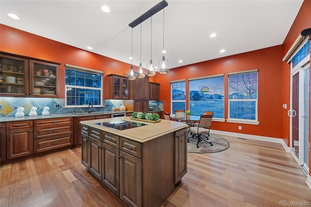 kitchen featuring light wood finished floors, decorative backsplash, glass insert cabinets, light countertops, and black electric cooktop