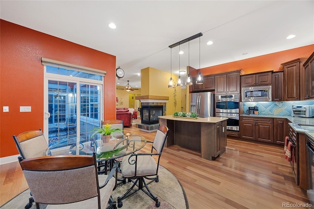 kitchen featuring a fireplace, dark brown cabinetry, light countertops, appliances with stainless steel finishes, and a center island