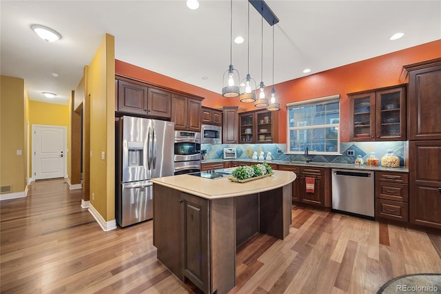 kitchen with backsplash, light wood-style flooring, appliances with stainless steel finishes, and glass insert cabinets