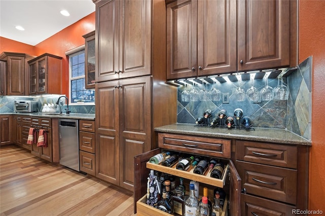 kitchen with a sink, glass insert cabinets, stainless steel dishwasher, light wood finished floors, and decorative backsplash