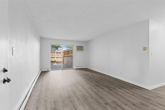 spare room featuring wood finished floors, a wall mounted air conditioner, a textured ceiling, a baseboard heating unit, and a baseboard radiator