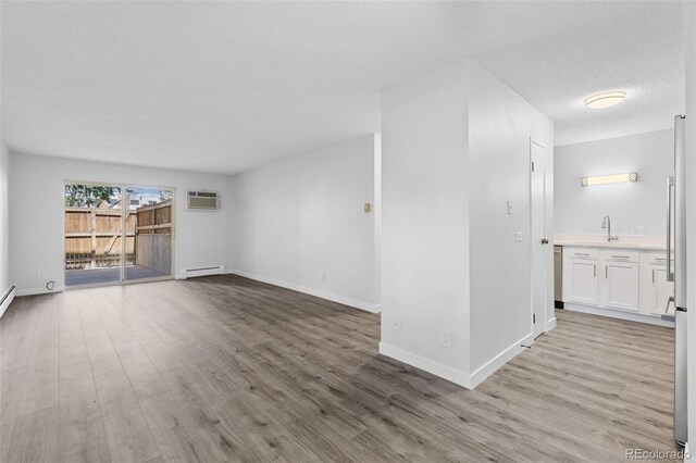 unfurnished living room featuring a baseboard radiator, light wood-style flooring, a wall unit AC, a textured ceiling, and baseboards