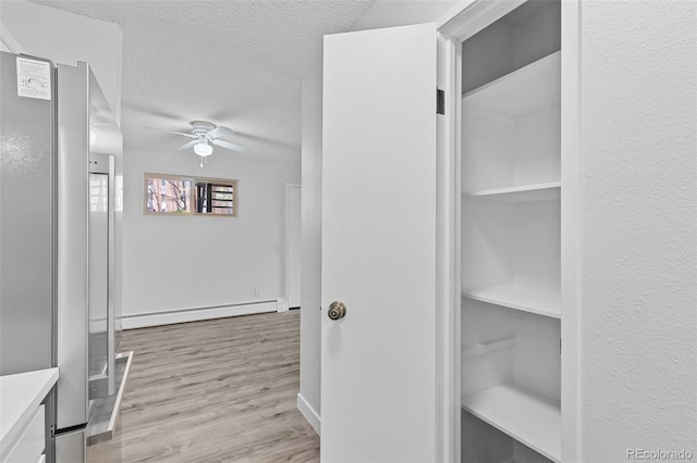 corridor with a textured ceiling, a baseboard heating unit, and light wood-style floors