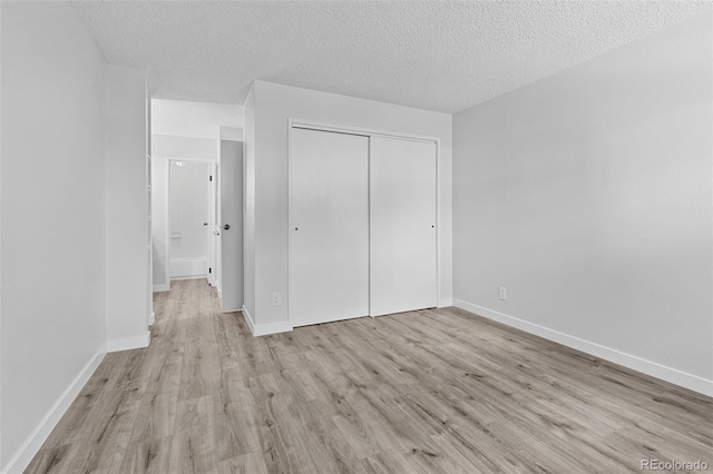 unfurnished bedroom featuring a textured ceiling, a closet, baseboards, and wood finished floors