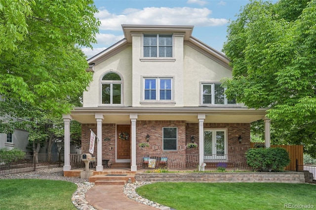 view of front of house with brick siding, fence, a front yard, a porch, and stucco siding