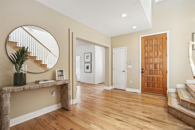 entryway with light wood-type flooring, baseboards, recessed lighting, and stairs