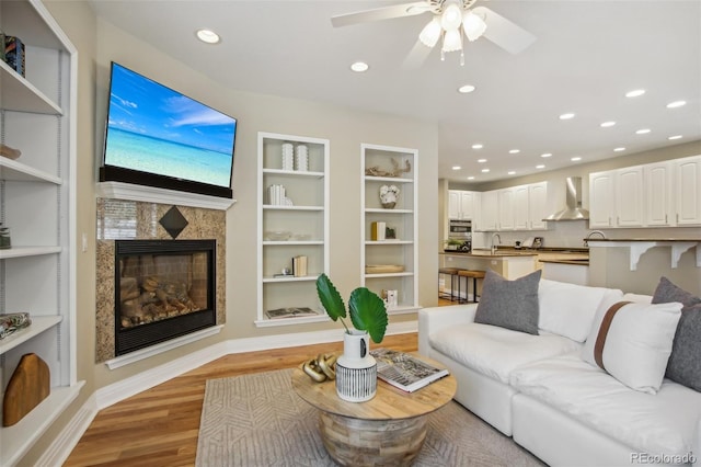 living room with built in shelves, recessed lighting, baseboards, light wood finished floors, and a tiled fireplace