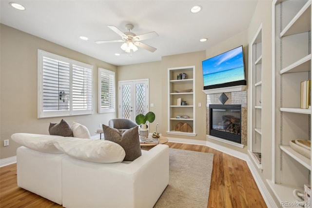 living area featuring built in features, recessed lighting, a glass covered fireplace, ceiling fan, and wood finished floors