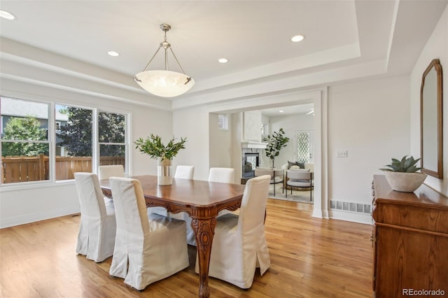 dining space featuring a high end fireplace, visible vents, baseboards, light wood-type flooring, and a tray ceiling