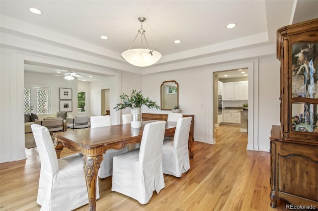 dining room with a tray ceiling, light wood-style flooring, and recessed lighting