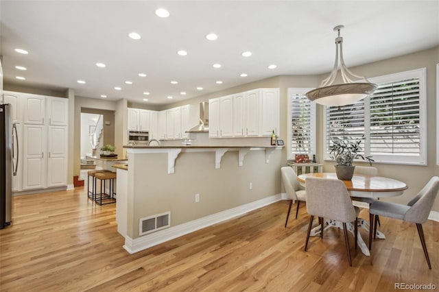 kitchen featuring visible vents, white cabinetry, a kitchen breakfast bar, light wood-type flooring, and wall chimney exhaust hood