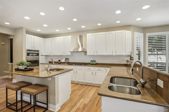 kitchen with wall chimney range hood, appliances with stainless steel finishes, a breakfast bar, and a sink